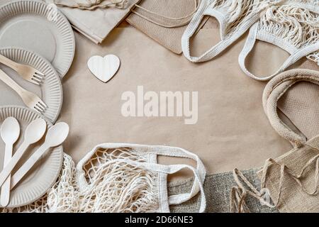 Frame made of eco-friendly set. Wooden heart and paper and mesh cotton eco bags, wooden cutlery, paper disposable tableware. Zero waste objects. Flat Stock Photo