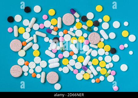 Different kinds of pills in different colors and sizes on a blue background. Top view, flat lay Stock Photo