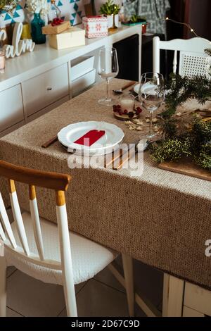 Homely christmas table setting, decorated with pine branches and rustic tablecloth in the living room of home in European style, with Christmas lights Stock Photo