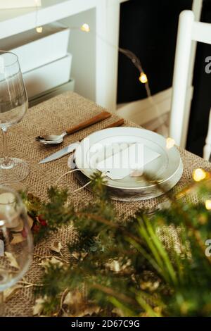 Holiday Gold place setting, Christmas table menu with empty card, ornaments and natural pine branch on rustic beige mantel, dinner at home Stock Photo