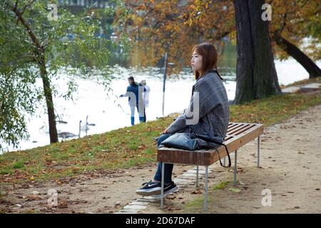 Asian woman alone stting on park seat next to Vltava river in Prague, Czech Republic Stock Photo