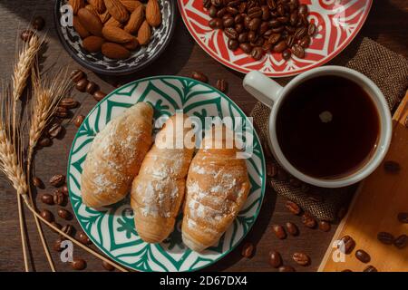 breakfast with breads and coffee on wooden table with coffee beans and almonds under daylight in plane Stock Photo