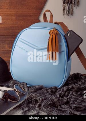 blue leather backpack on gray scarf with black cell phone on table with magazines with wooden background and white wall Stock Photo