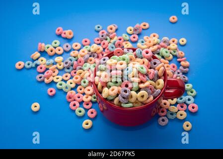 Bowl of Cereal, Colorful cereal in a bright red bowl on wood, cereal loops on a blue background. Quick breakfast or snack, flat lay. Stock Photo