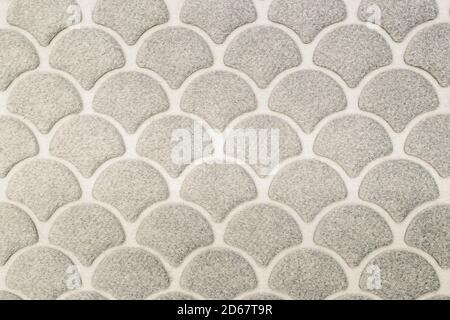Fragment of wool floor mat of semicircular leaves arranged in horizontal rows, overlapping each other on light backdrop. Natural textile background Stock Photo