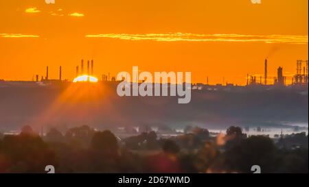 Scarlet sunrise over a chemical plant with pipes at the edge of a forest with a misty hollow Stock Photo
