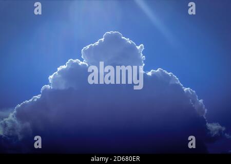 Gathering cumulus cloud with silver lining with sun rays overhead against an azure blue sky Stock Photo