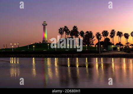 Sunset over illuminated Long Beach Lighthouse, palm trees and grassy area at ShoreLine Aquatic Park, with shimmering reflections in the water. Stock Photo