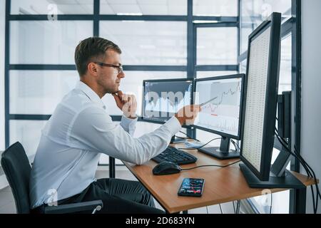 Analysing graphs. Young businessman in formal clothes is in office with multiple screens. Conception of exchange and money Stock Photo