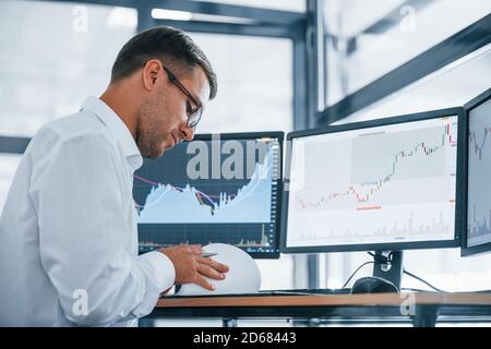 Works with documents. Young businessman in formal clothes is in office with multiple screens. Conception of exchange and money Stock Photo