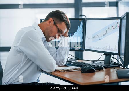 Works with documents. Young businessman in formal clothes is in office with multiple screens. Conception of exchange and money Stock Photo