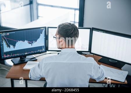 Busy employee. View from the back. Young businessman in formal clothes is in office with multiple screens. Conception of exchange and money Stock Photo