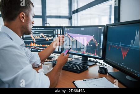 Young businessman in formal clothes is in office with multiple screens. Conception of exchange and money Stock Photo