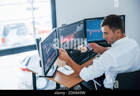 Young businessman in formal clothes is in office with multiple screens. Conception of exchange and money Stock Photo