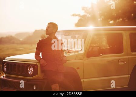 Portrait of man that leaning on green car at beautiful sunny day outdoors in the field Stock Photo