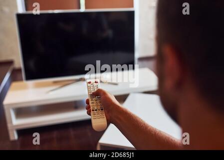 Backing view of man holds remote controller in hand and turning on TV Stock Photo