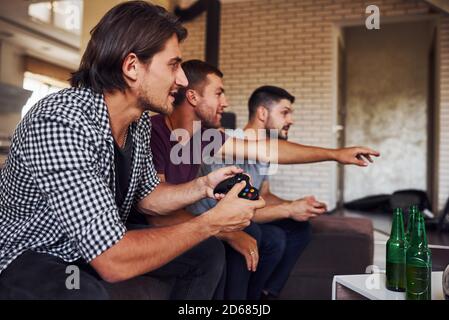 Side view. Group of friends have fun playing console game indoors at living room Stock Photo