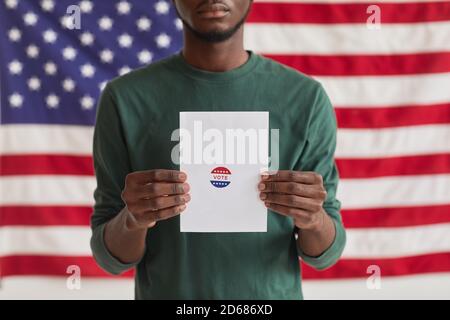 Portrait of Afro-American man holding ballot with Vote sign while standing against the American flag Stock Photo