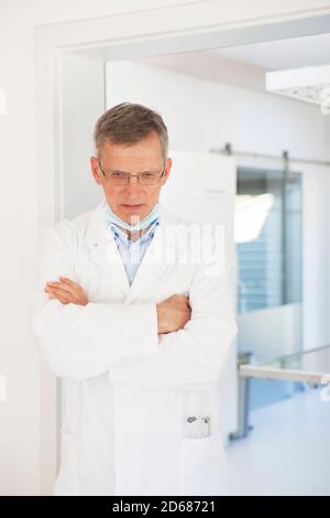 Tired and sad mature doctor standing in front of his surgery - selective focus Stock Photo