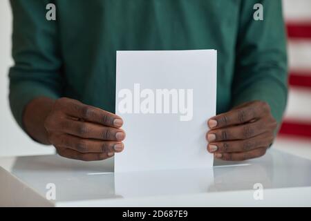 Close-up of Afro-American voter holding ballot standing near the ballot box Stock Photo