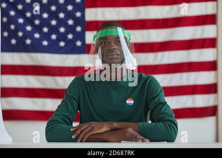 Portrait of Afro-American man wearing protective mask sitting at the table and voting for American flag Stock Photo