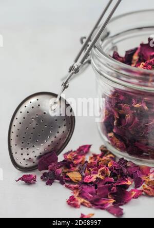 Rose petals craft grade tea in glass jar with vintage strainer infuser on white background. Stock Photo