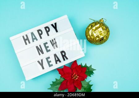 Happy new year light box with golden bauble and poinsettia on blue background Stock Photo