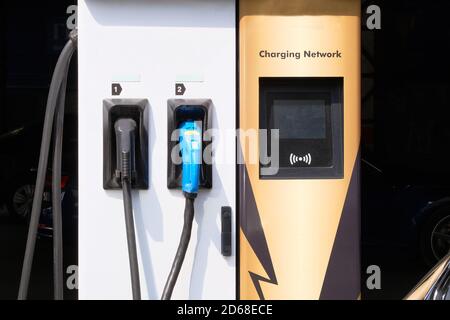 Electric charging station. Car electric charger station installed near iron metal fence near parking lot. Eco friendly transport concept. Stock Photo