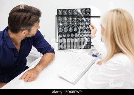 doctor explains to man patient the results of an MRI scan of his brain. Diagnosis of diseases and head injuries. Headache treatment Stock Photo