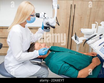 Dentist examining a male patient using a special microscope in a modern dental clinic Stock Photo