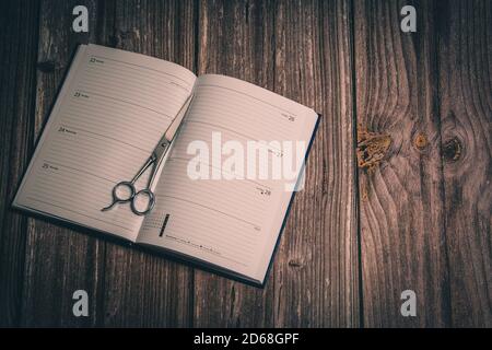 A pair of hairdressing scissors laid on an open diary laid on a rustic wooden table Stock Photo