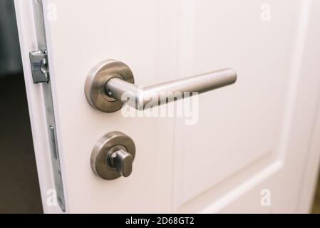 Open the white door. Modern chrome handle in your hotel room or home. Entrance to an apartment, office, or bedroom. Door detail. Interior of a house o Stock Photo