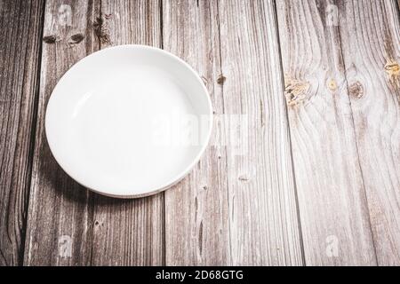 an empty plain white bowl on a rustic wooden dining room table Stock Photo