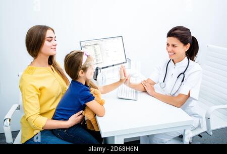 Friendly pediatrician woman give high five to child patient, small girl and her mother at the medical exam Stock Photo