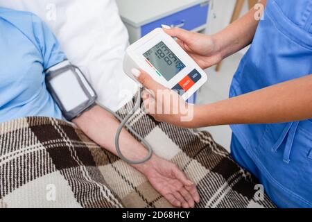 Nurse measures the pressure of an elderly woman patient who is lying on a hospital bed. Women have very high blood pressure, hypertension. Prevention Stock Photo