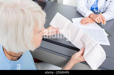 Elderly patient looking at the results of a cardiogram of her heart in a cardiologist's office. Diagnostics and treatment of arrhythmias, coronary hea Stock Photo