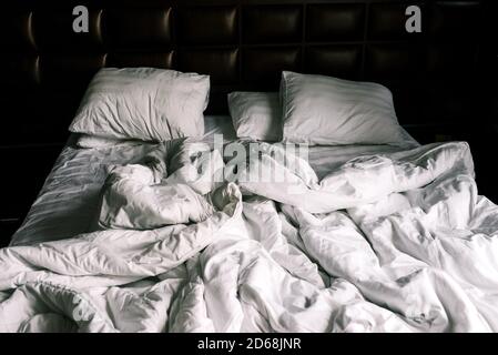 Unmade double empty bed with white linens. Sheets and pillows in the apartment or hotel after a night's sleep. The bed was dirty and unmade. Rumpled Stock Photo