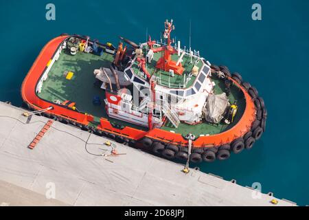 Tug boat with  bright orange hull and green deck is moored in a port. Aerial view Stock Photo
