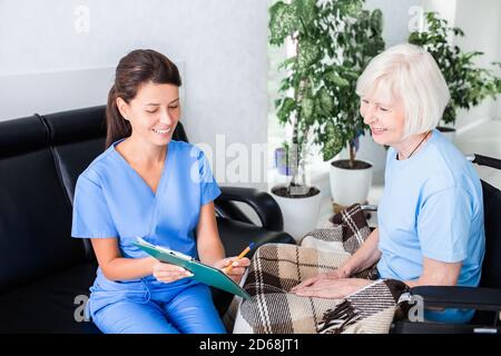 Nurse shows test results to an elderly patient who is sitting in a wheelchair, tests are normal. Rehabilitation of people after injuries and illnesses Stock Photo
