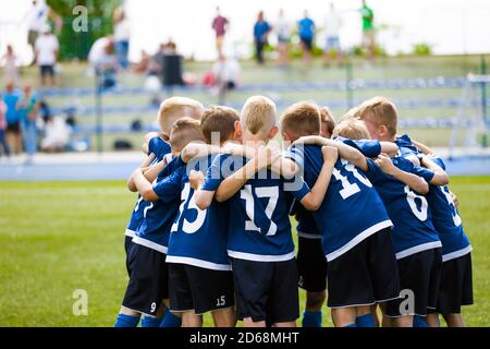 Boys football team forming huddle. Happy kids in a sports team on grass pitch. Summer school soccer tournament. Children playing sports outdoor Stock Photo