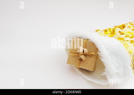 Gift box wrapped in kraft paper and tied sack rope in yellow christmas sock on white background Stock Photo