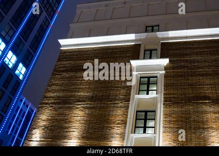Part of the facade of a brick building with windows on the background of modern high-rise buildings at night Stock Photo
