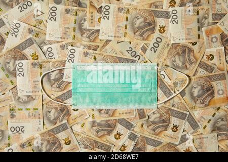 Lots of 200 zloty bills with a medical protective mask on them. Conceptual image about the stability of the economy in Poland. Stock Photo