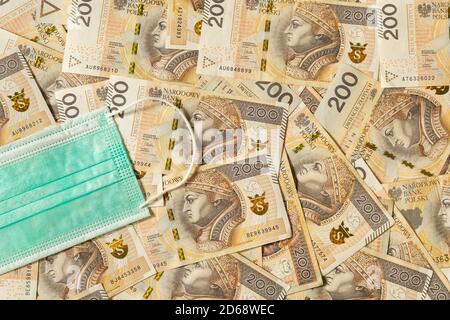 Lots of 200 zloty bills with a medical protective mask on them. Conceptual image about the stability of the economy in Poland. Stock Photo