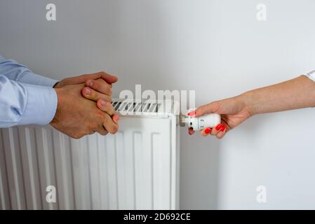 Woman Hand Adjusting The Knob Of Heating Radiator. A hand that regulates the temperature in the radiator and male's hands rubbed with cold. Hands warm Stock Photo