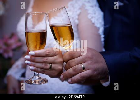 detail hands of wedding couple wearing golden wedding rings and glass bowl containing alcohol drink Stock Photo