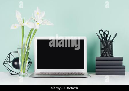 Fresh home workspace with blank laptop monitor, black stationery, books, abstract modern sculpture, white spring flowers in green mint menthe interior Stock Photo