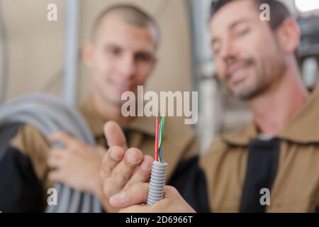 builders looking at the cables coming out of grey trunking Stock Photo