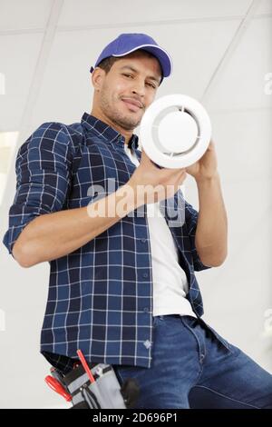 handsome young man electrician cleaning air filter on a ladder Stock Photo