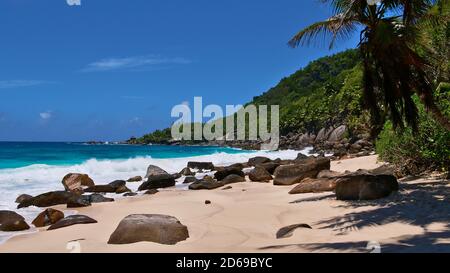 Remote tropical beach Anse Capucins in the south of Mahe island, Seychelles with sand, rainforest and waves hitting the granite rock formations. Stock Photo
